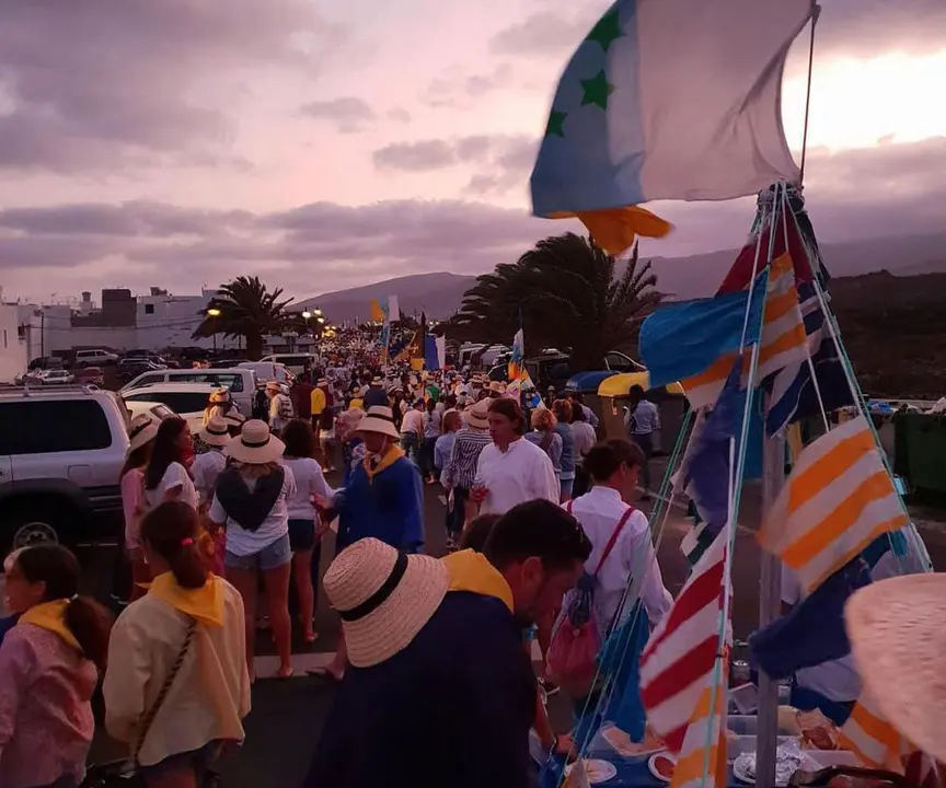 Romería de las Fiestas del Pino 2025 en Punta Mujeres al atardecer Multitud en la romería de las Fiestas del Pino 2025 en Punta Mujeres al atardecer, con banderas canarias y ambiente festivo.