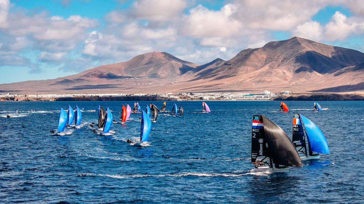 Regata de vela frente a Playa Blanca en Lanzarote en marzo, con volcanes al fondo y veleros con spinnakers de colores