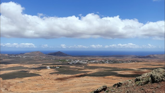 Playa de Costa Teguise en abril con tumbonas, sombrillas y aguas turquesas sobre roca volcánica en un día soleado