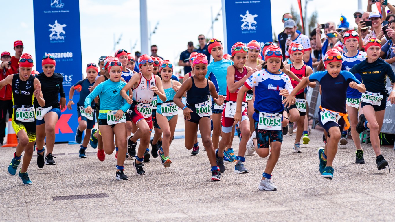 Niños corriendo en la salida del IRONMAN Kids Lanzarote con dorsales y gorros de natación